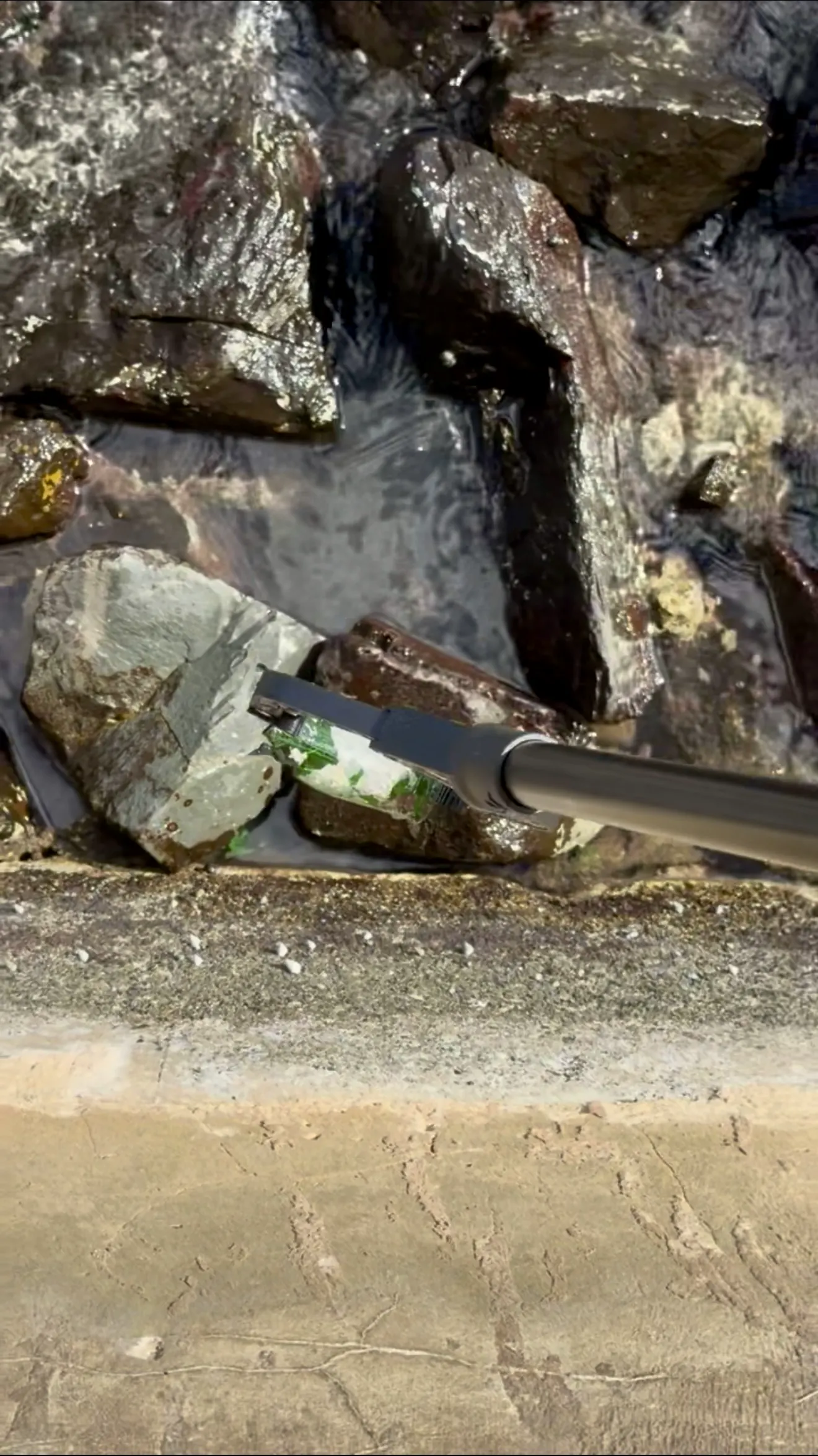 CRFF team member removing a glass bottle from rocky shoreline with a grabber